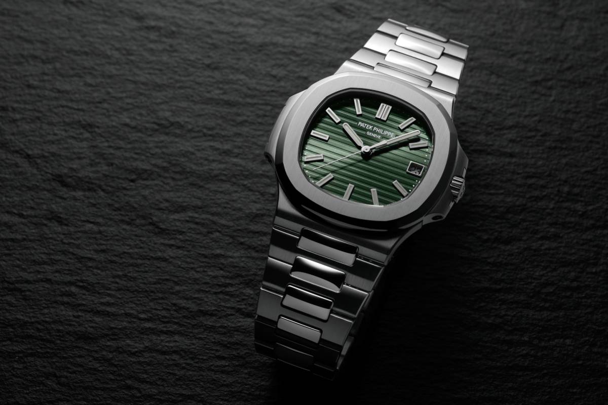 Primo piano dell'orologio di lusso Patek Philippe Nautilus con quadrante verde e cassa in acciaio inossidabile, su sfondo scuro.