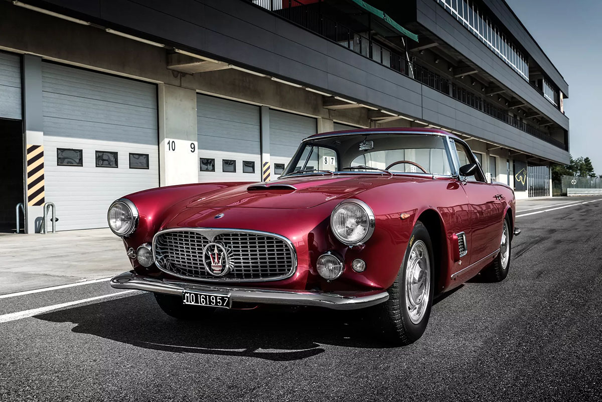 Maserati 3500 GT rossa parcheggiata davanti a un garage di pista, simbolo dell'eleganza e della storia del marchio Maserati.