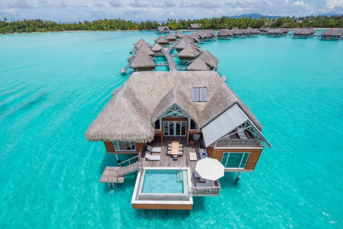 Vista aerea di un lussuoso bungalow sull'acqua in un resort di Bora Bora, circondato da acque turchesi cristalline, simbolo di lusso e relax.