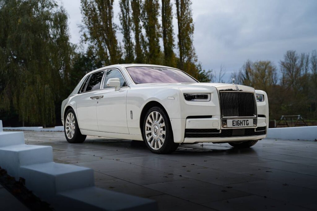 Rolls-Royce Phantom bianca, simbolo di lusso e artigianato britannico, con dettagli esclusivi e design senza tempo, esposta all'aperto su una piattaforma.