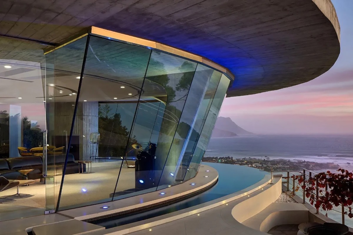 Villa di lusso moderna con ampie vetrate e vista panoramica sull'oceano al tramonto, esempio di architettura di alto design e fascino cinematografico.